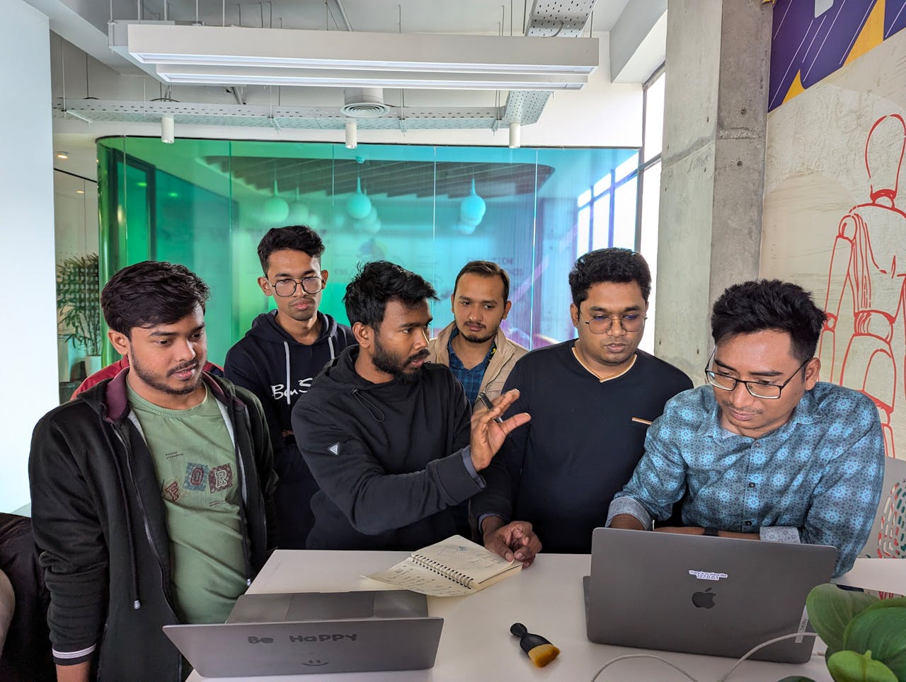 Group of colleagues collaborating in a modern office setting, engaging in a discussion around a laptop.